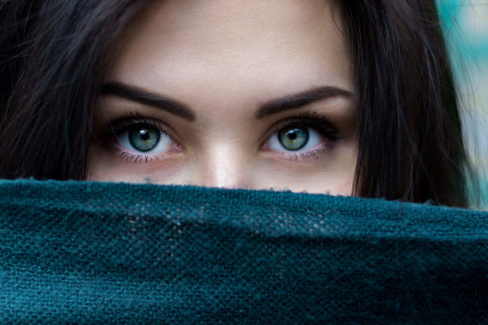 A woman's eyes, with half of her face covered by a piece of blue fabric