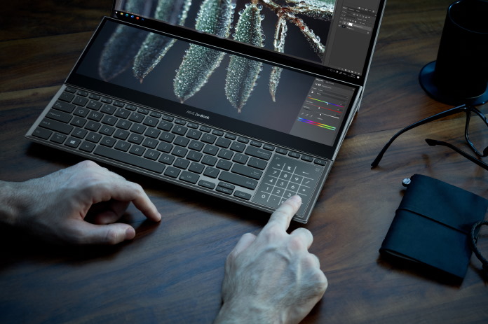 A man using the dual-screen Zenbook Pro Duo 15 OLED laptop for image editing with Adobe Lightroom on a desk with other creative gear