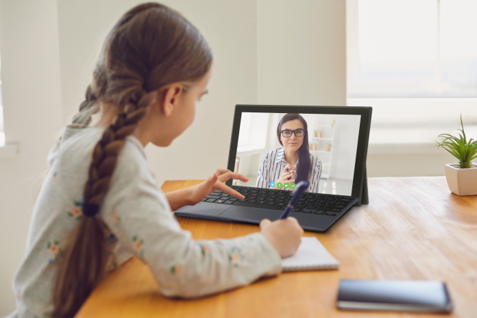 A schoolgirl teleconferencing with her instructor using a detachable laptop