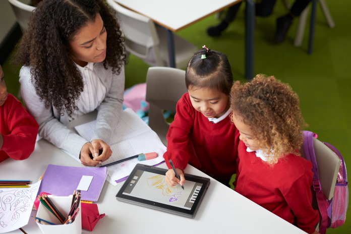 Woman working with two school-age children who are using a convertible laptop and a stylus