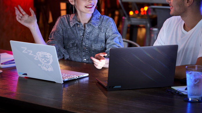 Young man and woman talking at a table in front of ROG Zephyrus G14 and M16 laptops