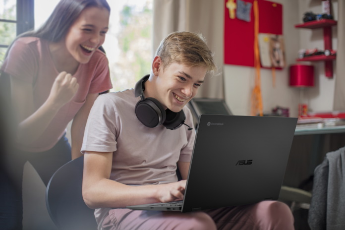 Happy teenage girl watching boy using laptop - Edge Up