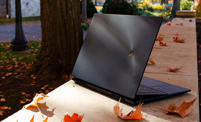 Zenbook Pro 16X OLED laptop sitting on a stone retaining wall covered with autumn leaves