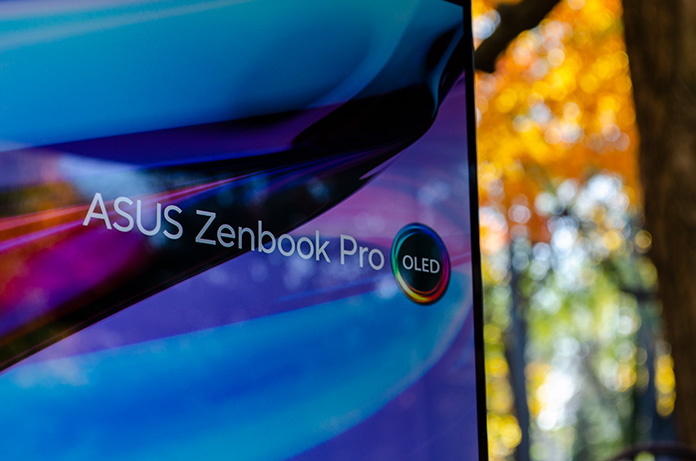 The Zenbook Pro 16X OLED laptop sitting on a stone wall in front of trees