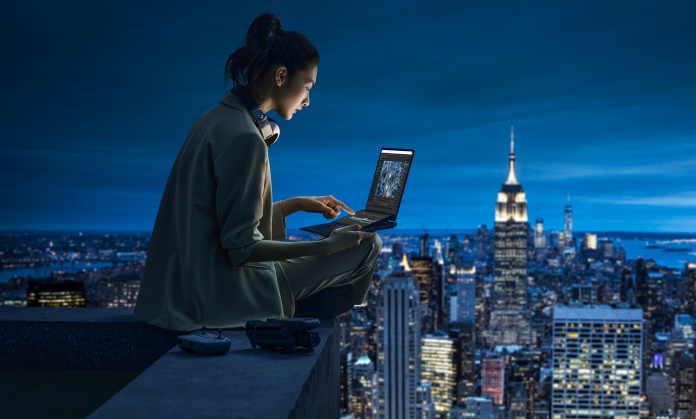 Young woman editing photos on the Zenbook Pro 14 Duo OLED laptop while sitting atop a tall building
