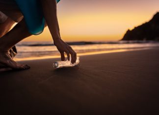 Person picking up a plastic bottle along a beach at sunset