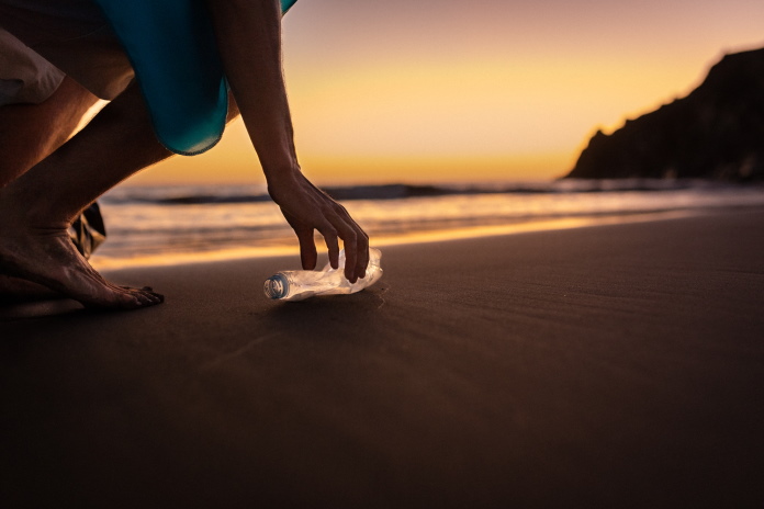 Person picking up a plastic bottle along a beach at sunset