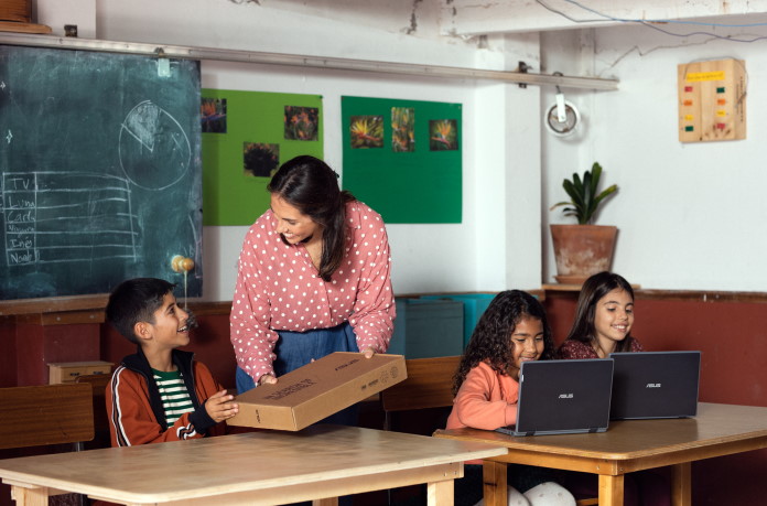 Woman handing a laptop box to a child in a classroom