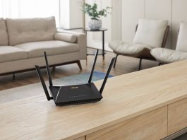 An ASUS extendable router on a low table in a living room with couch and chairs behind