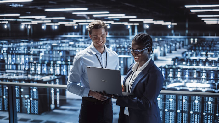 A man and a woman in front of a room of servers look at data together on an ExpertBook laptop