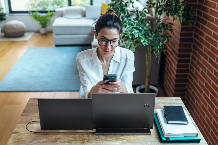 A woman sitting a desk with an ASUS portable monitor and laptop