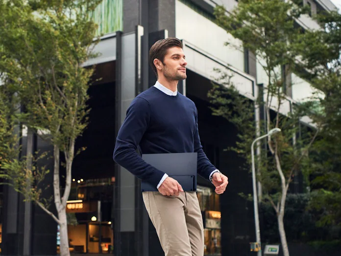 A man walking along a city street holding an ASUS portable monitor in one hand