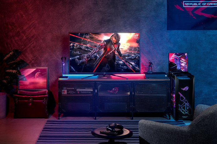 A gaming den with a comfy chair, large gaming monitor, and a gaming PC in the ROG Strix Helios case