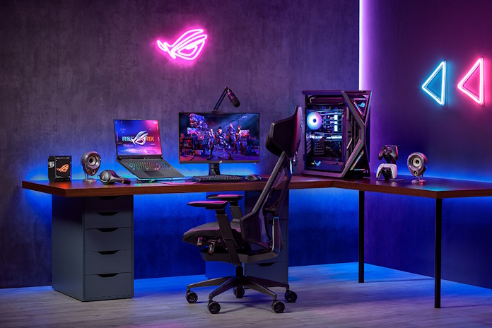 A gaming desk with an ROG laptop on a stand, a desktop PC, controller, headset, and a DIY PC