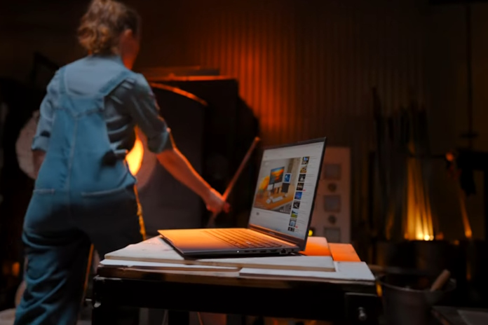 An ASUS laptop being used in an industrial setting with high heat and a woman working at a forge in the background 