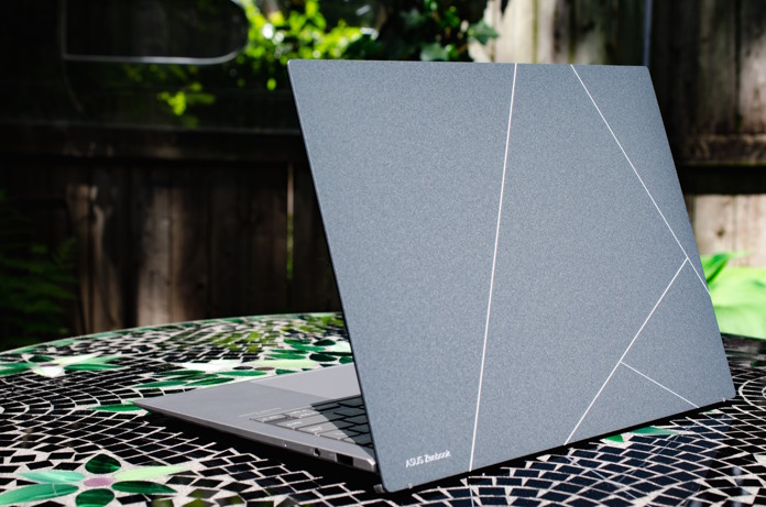 A view of the Zenbook S 13 OLED's lid on a stone table in a backyard full of greenery