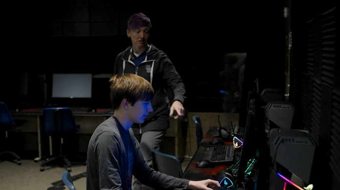 The esports coach at Oswego High School giving a student instruction as he practices using an ROG GL12CX gaming desktop PC