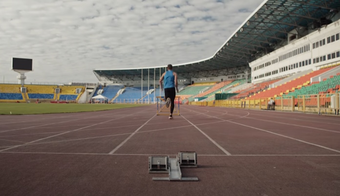 A high school student practicing hurdles in an empty stadium