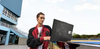 A young man uses his Vivobook S 15 OLED BAPE Edition laptop as it sits on a railing outside an urban building