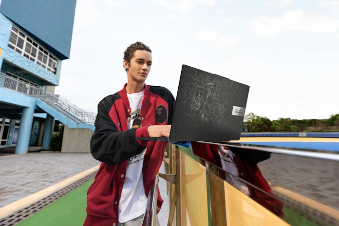 A young man uses his Vivobook S 15 OLED BAPE Edition laptop as it sits on a railing outside an urban building