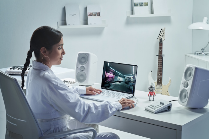 A woman at a desk with an ROG Zephyrus G14 laptop with musical isntruments int he background and streaming equipment nearby
