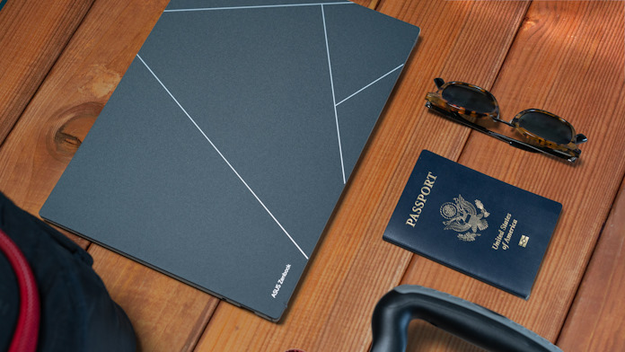 The Zenbook S 13 OLED laptop on a table with a passport and sunglasses and other items commonly taken when traveling abroad