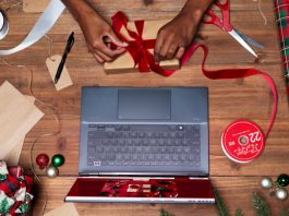 A person wrapping up a present with brown paper and red ribbon on a wooden table in front of a Zenbook laptop