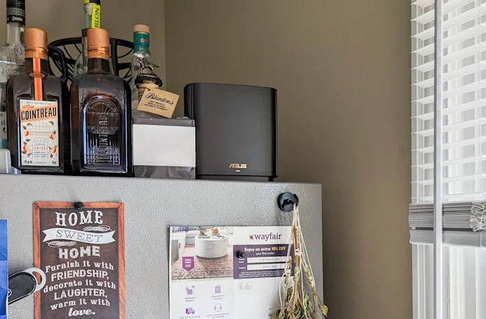 The ZenWiFi XT8 mesh WiFi system on top of a refrigerator with assorted bottles and a nearby window