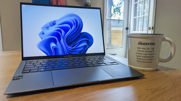 The Zenbook S 13 OLED laptop on a table inside with a coffee cup nearby on the table