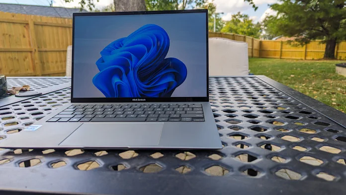 The Zenbook S 13 OLED laptop on a metal table in the fenced-in back yard of a house 