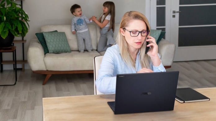 A woman doing a conference call at her computer while her children play on the couch behind her