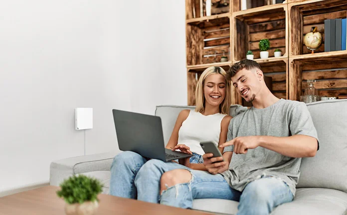 A young man and woman sitting on a couch together using a travel router to keep their devices connected