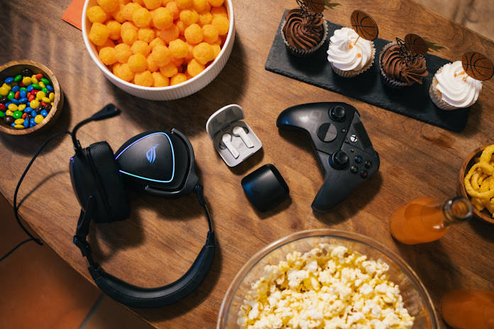 An ROG headset, headphones, and an Xbox controller on an end table full of March Madness party food and drinks