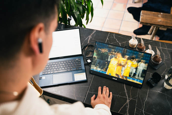 A young man watches basketball using a ZenScreen portable display connected to an ASUS Zenbook laptop