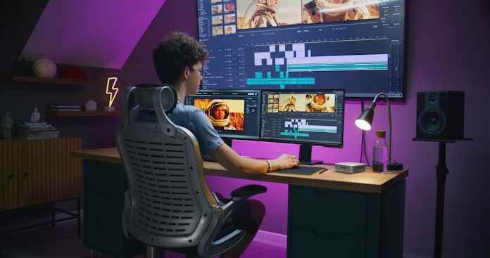 A young man doing video editing at a three-monitor creative workstation powered by an ASUS NUC