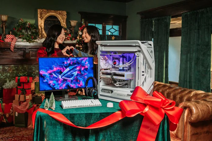 Two young women making a heart symbol with their hands as they stand behind a completed gaming PC setup 