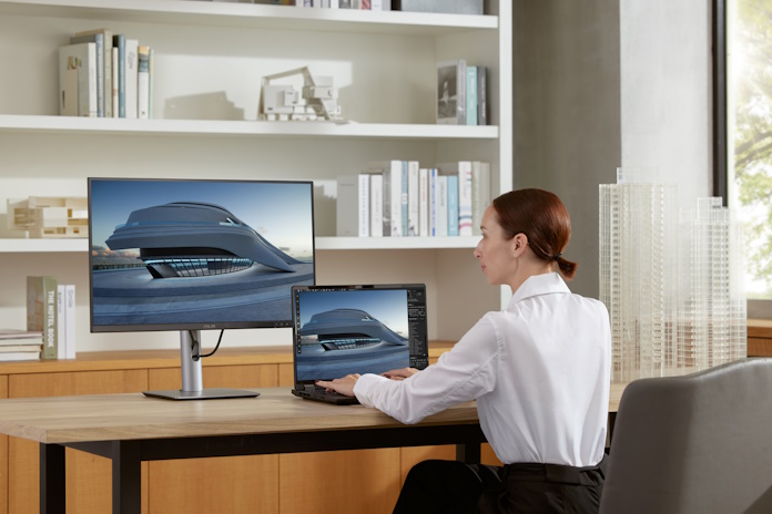 An artist editing a 3D asset using a laptop and a 32-inch display