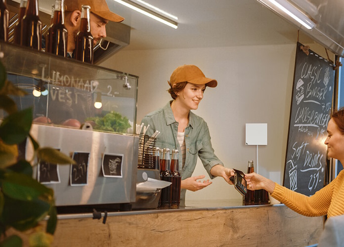 A woman serves a customer at a cafe with an ASUS travel router on the wall nearby