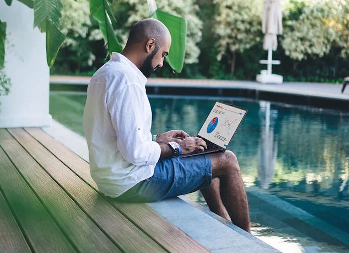 A man works on his laptop with his feet cooling off in a pool