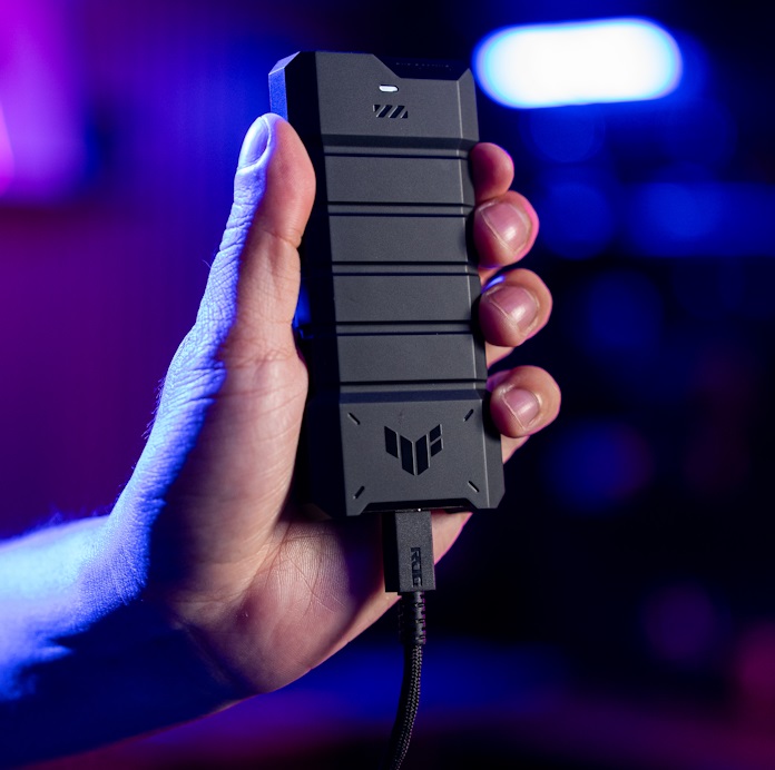 A man holding up the TUF Gaming A2 portable SSD enclosure with a cable attached