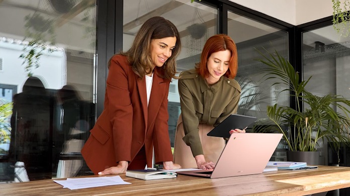 Two women in an office environment work together using an ASUS laptop