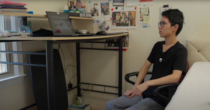 A young man sits at a desk raised up off the floor with books, on which is sitting a laptopp