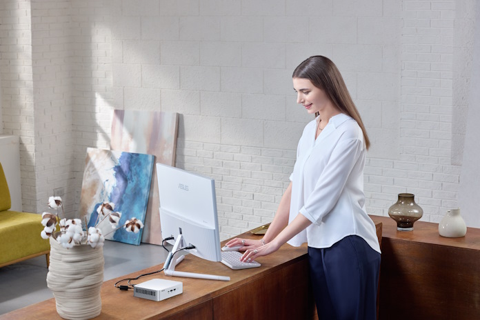 A woman stands at a desk using an ASUS smart monitor and an ASUS NUC 15 Pro 