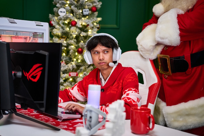 A young man looks suspiciously at Santa while gaming at his desk